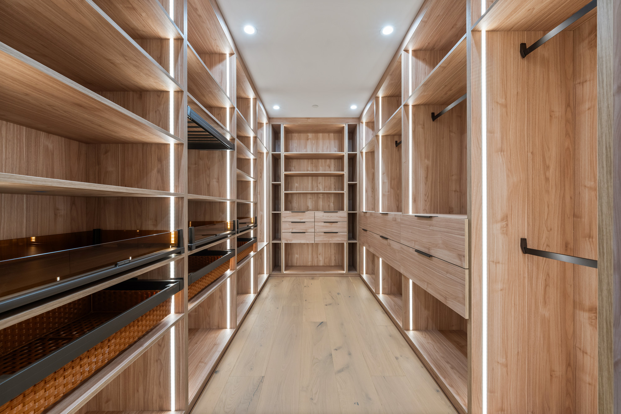 White oak walk-in closet with backlit shelving and leather-lined drawers